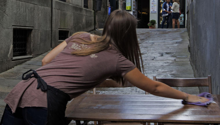 A waitress cleans a table in front of a balcony with a Galician type flag with a black ribbon signalling mourning as life gets back to normal in Santiago de Compostela, Spain, Saturday July 27, 2013. Spain's interior minister Jorge Fernandez Diaz says the driver whose speeding train crashed, killing 78 people, is now being held on suspicion of negligent homicide. The Spanish train  derailed at high speed Wednesday killing 78 and injuring dozens more. (AP Photo/Lalo R. Villar)